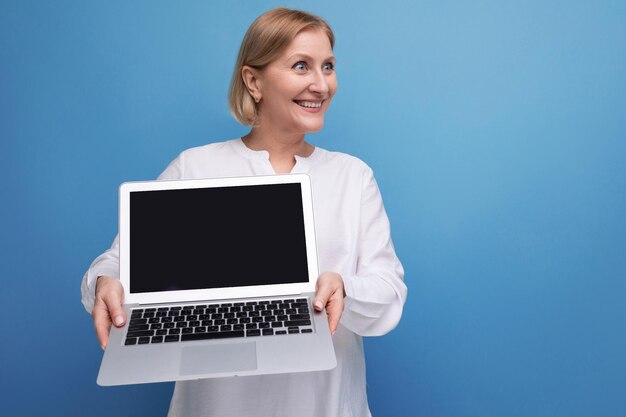 Portrait of happy middle aged business woman with blond hair using laptop with mocup