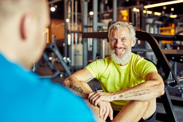 Портрет счастливого мужчины средних лет, обсуждающего результаты тренировок с фитнес-инструктором или персоналом