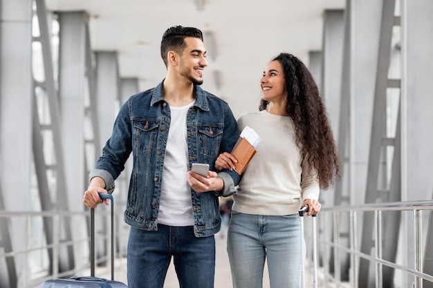 portrait of happy middle eastern couple walking at airport with luggage