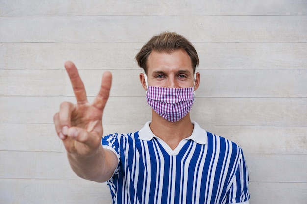 Portrait of happy millennial man smiling with thumbs up while wearing medical protective mask for coronavirus spread prevention