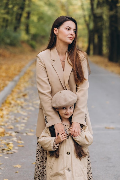 Portrait of happy mother and daughter spending time together in autumn park with falling yellow leaves