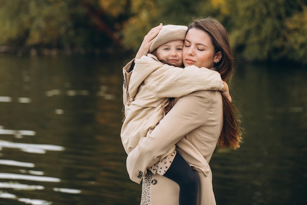 Portrait of happy mother and daughter together in autumn park with falling yellow leaves near lake