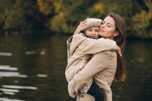 Ritratto di madre e figlia felici insieme nel parco autunnale con foglie gialle che cadono vicino al lago