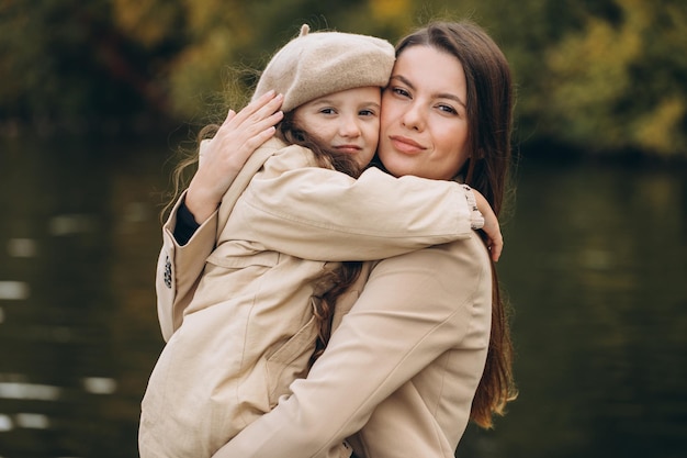 Photo portrait of happy mother and daughter together in autumn park with falling yellow leaves near lake