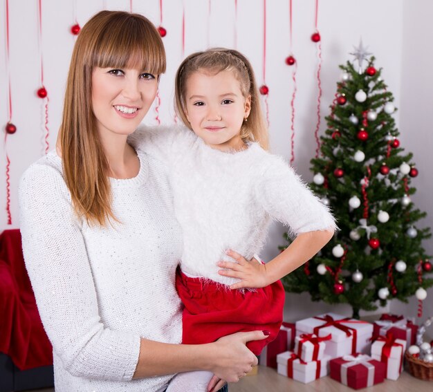 Portrait of happy mother and daughter with Christmas tree at home