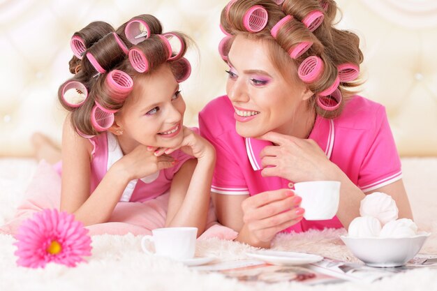 Portrait of happy  Mother and little daughter in hair curlers with magazine at home