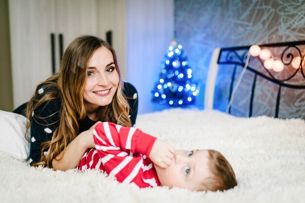 Portrait of happy mother and son celebrate Christmas. New Year's holidays. Toddler with mom in the festively decorated room with Christmas tree and decorations.