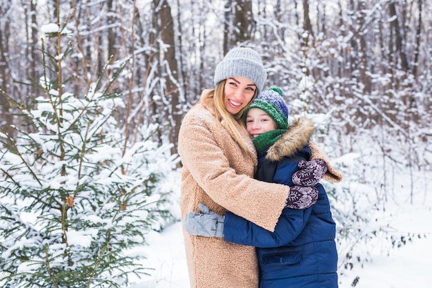 Portrait of happy mother with child son in winter outdoors. Snowy park. Single parent.