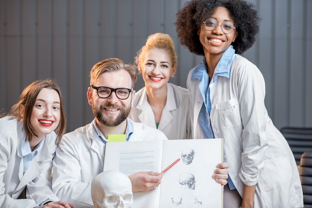 Ritratto di un felice gruppo multietnico di scienziati medici o studenti seduti insieme a un libro in ufficio o in classe