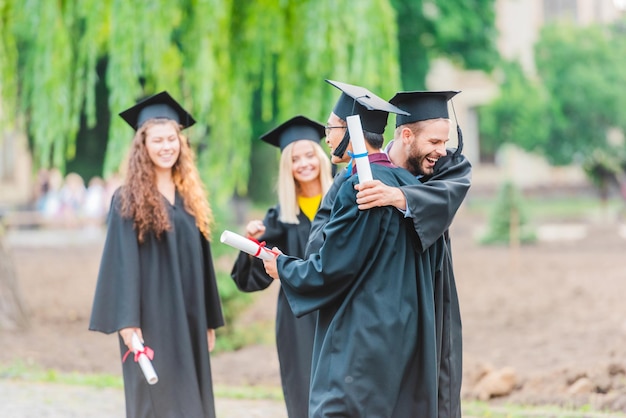 portrait of happy multiracial graduates with diplomas on street