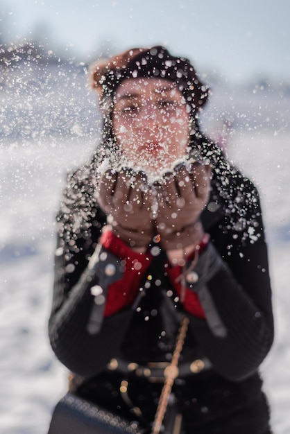 Portrait of a happy Muslim woman in winter fashion hijab blowing snow outside.