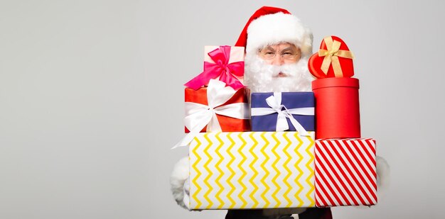 Portrait of happy old Santa Claus in eyeglasses while he packing and preparing gifts and presents in colorful gift boxes in studio