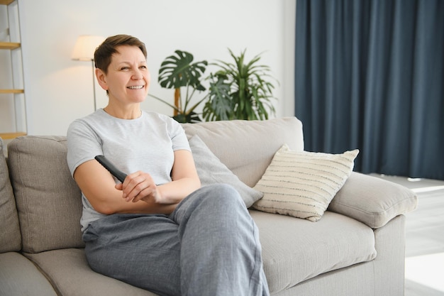 Portrait of happy older woman changing channel on television