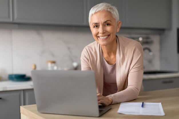 Portrait of happy older woman posing at laptop computer indoor