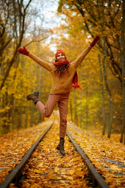 Portrait of happy overjoyed woman in jump over railroad in autumn forest. Excitement and fall weather