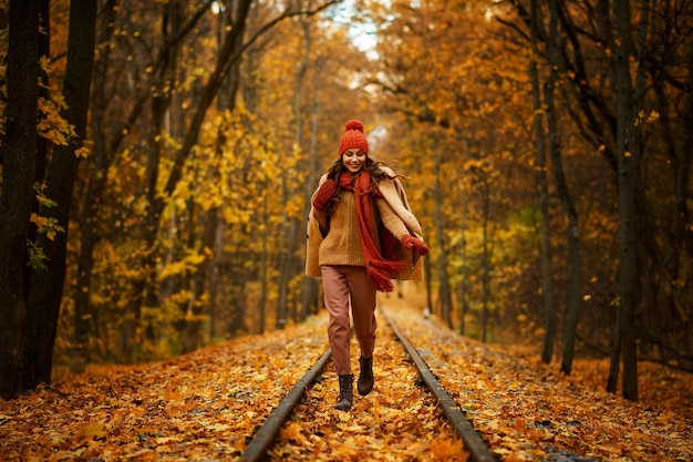 Portrait of happy overjoyed woman walking along railroad in autumn forest. Excitement and fall weather