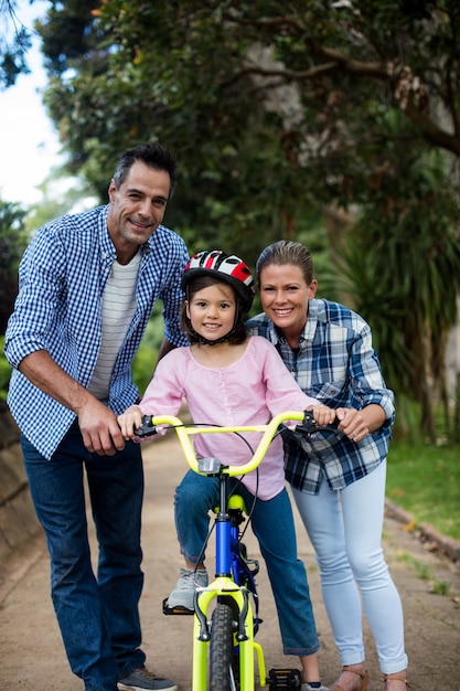 Ritratto dei genitori felici che assistono la figlia per guidare bicicletta in parco