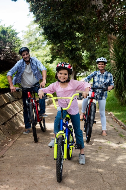 Portrait of happy parents and daughter standing with bicycle in park