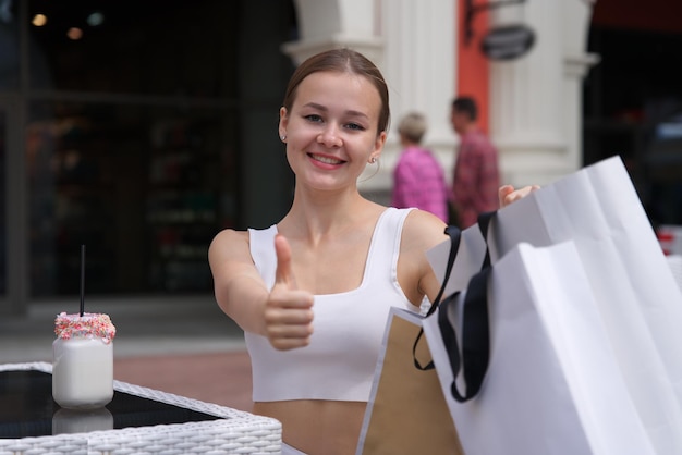 Portrait of happy positive stylish girl young teen teenager beautiful woman is smiling having fun in mall during shopping carrying holding shopping paper bags in hand