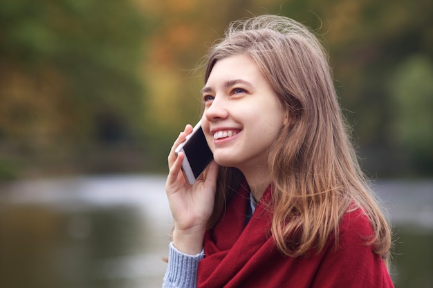 チャット、彼女の携帯電話のスマートフォンで話し、良いことを持っている幸せなポジティブな若い女性の肖像画