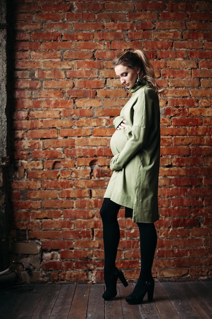 Portrait of happy pregnant brunette girl posing against brick wall