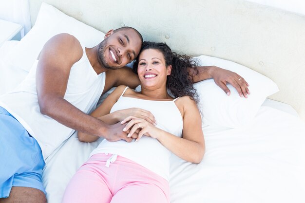 Портрет счастливой беременной жены с мужем, лежа на кровати