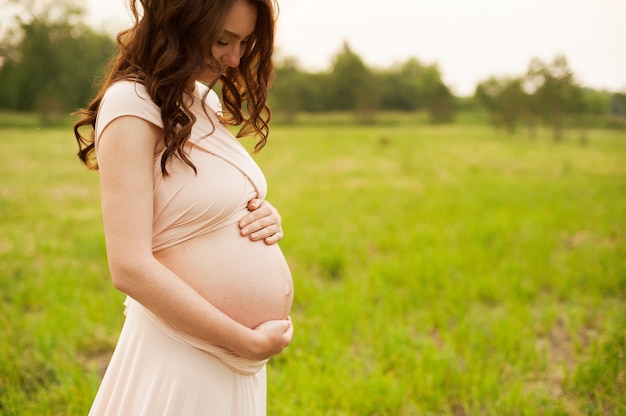 Portrait of a happy pregnant woman looking at her belly in a park at sunrise 