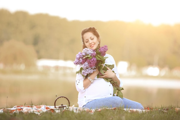 Portrait of happy pregnant woman with bouquet of lilacs on a pic