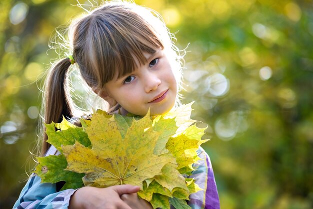 Portrait of happy pretty child girl holding a bunch of fallen
tree leaves in autumn forest