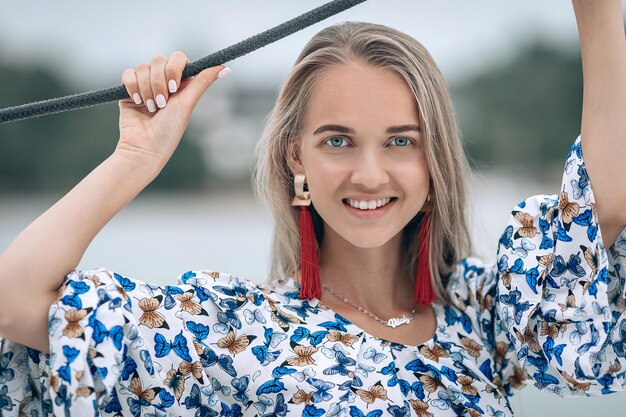 Portrait of happy pretty girl with colorful dress and long curly blonde hair sitting on yacht at summertime. looking at camera with toothy smile. Close up photo