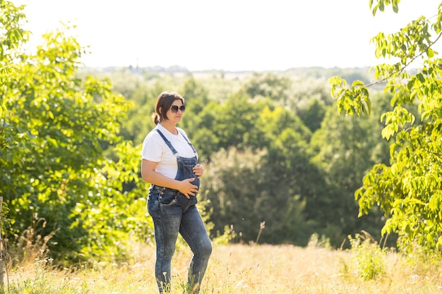 Ritratto di una donna incinta felice e orgogliosa che guarda il suo ventre in un parco all'alba con una calda luce posteriore sullo sfondo