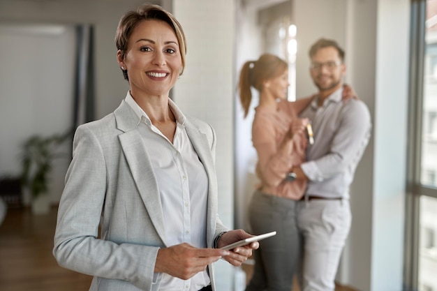 Portrait of happy real estate agent with a couple in the background