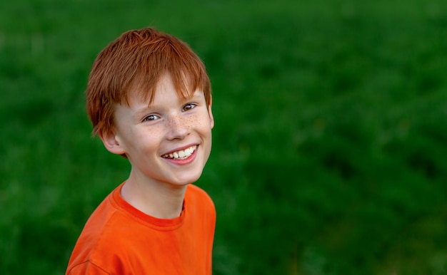 Portrait of a happy redhaired boy on a background of green grass