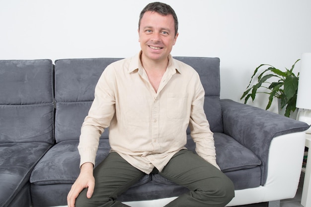Портрет счастливого и расслабленного мужчины, сидящего на диване в доме