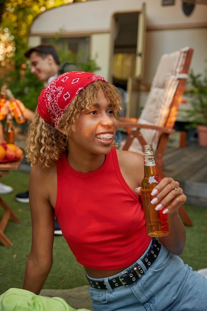 Portrait of happy relaxed millennial girl drinking beer while rest at campsite with friends. Holiday vacation trip concept