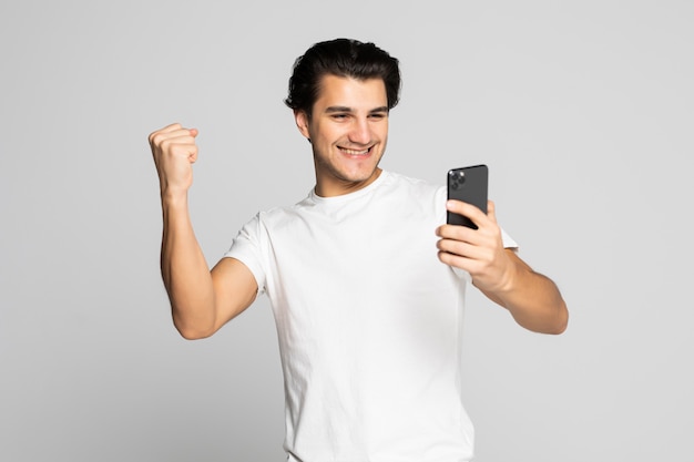 Портрет счастливого довольного человека, смотрящего на мобильный телефон и кричащего на белом