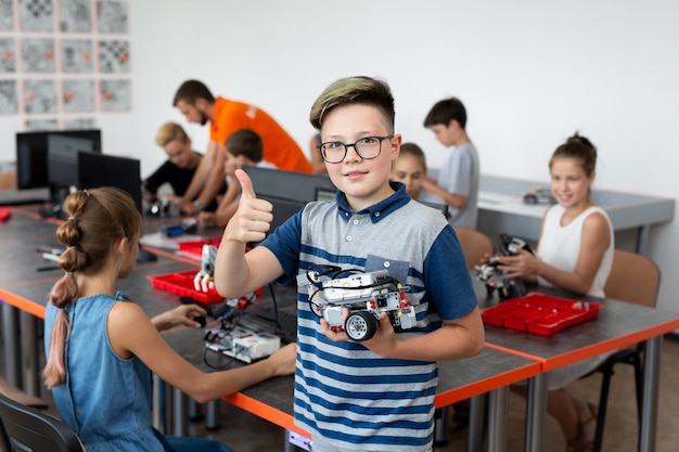 Portrait of a happy schoolboy boy with a robot that he himself assembled in robotics lessons at school, the boy shows a thumb up