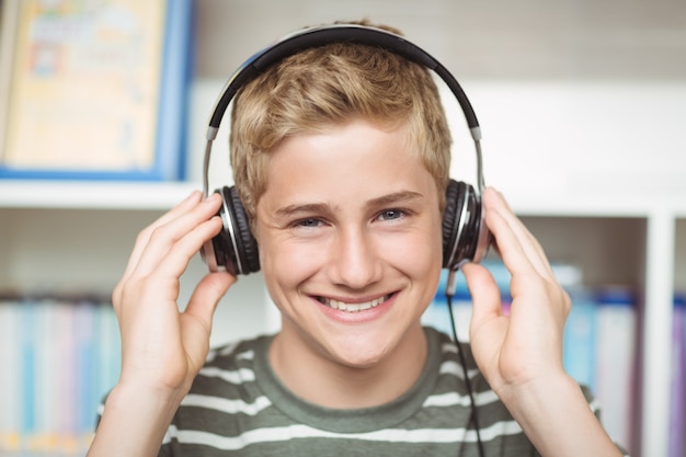 Portrait of happy schoolboy listening music on headphones in library