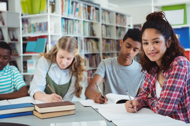 Ritratto di studentessa felice che studia con i suoi compagni di classe in biblioteca