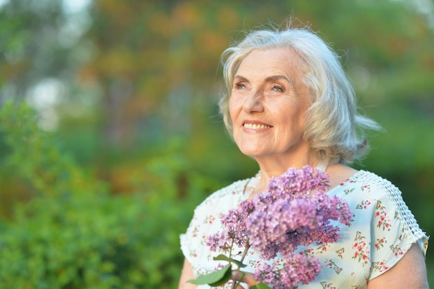 Portrait of happy senior beautiful woman with lilacs posing in spring park