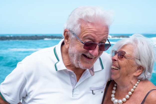 Portrait of happy senior couple hugging standing near beach enjoying beach vacation and freedom