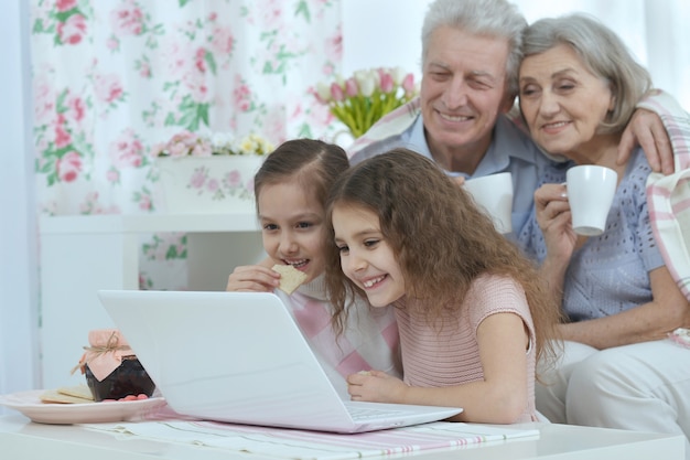 Portrait of a happy senior couple with grandchildren and laptop at home