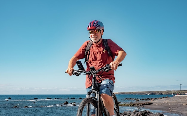 건강하고 건강한 활동적인 노인 남성이 되기 위해 바다에서 자전거를 타는 것을 즐기는 행복한 노인의 초상