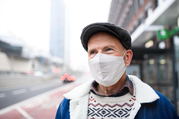 街の通りに屋外で立っている幸せな年配の男性の肖像画。コロナウイルスの概念。