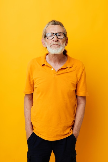 Portrait of happy senior man with a gray beard in glasses yellow background