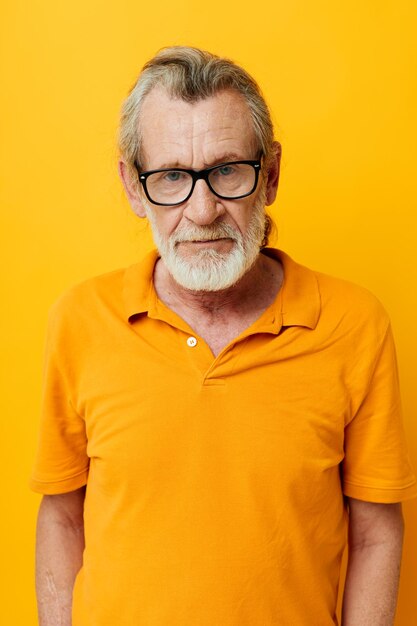 Portrait of happy senior man with a gray beard in glasses yellow background