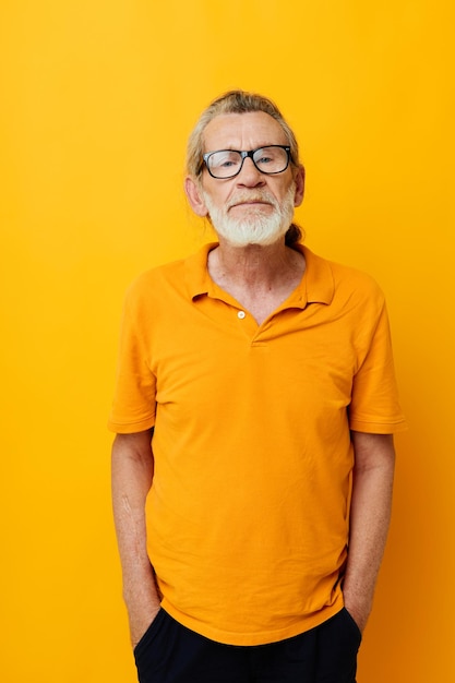 Portrait of happy senior man with a gray beard in glasses yellow background