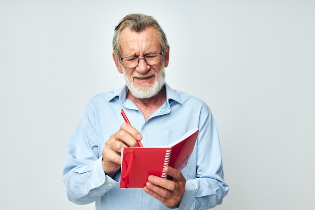 Portrait of happy senior man writes down emotions in a notebook light background