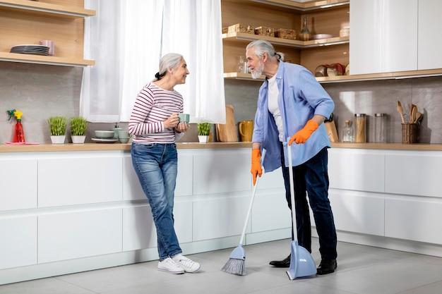 Photo portrait of happy senior spouses making cleaning in kitchen together