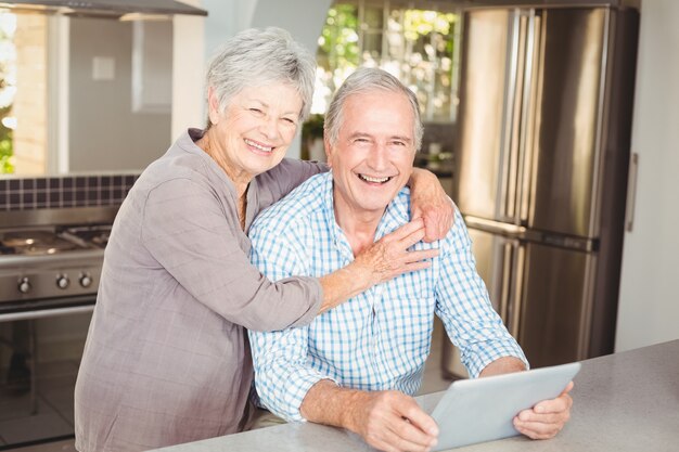 Portrait of happy senior woman embracing man with tablet